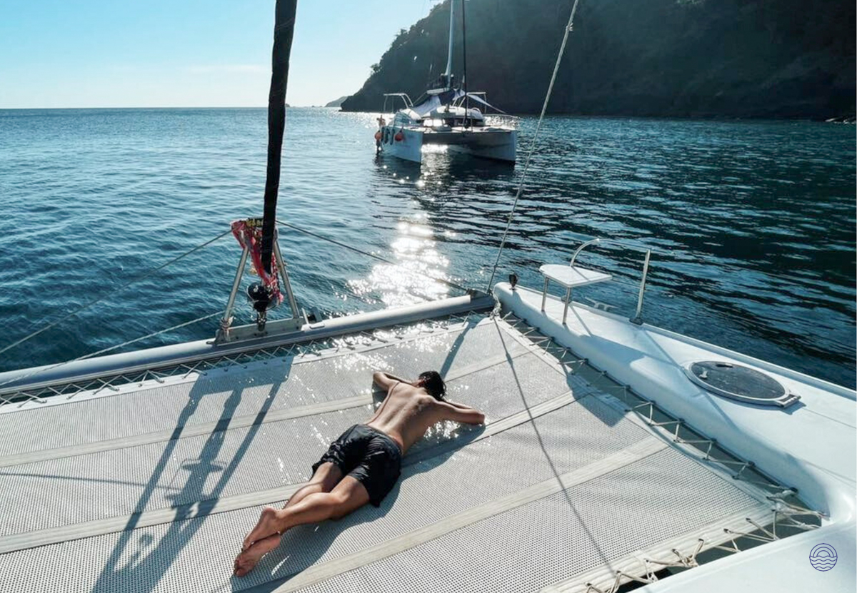 A person relaxes on a catamaran net, enjoying the sun and splashes in the Andaman Sea near Phuket.