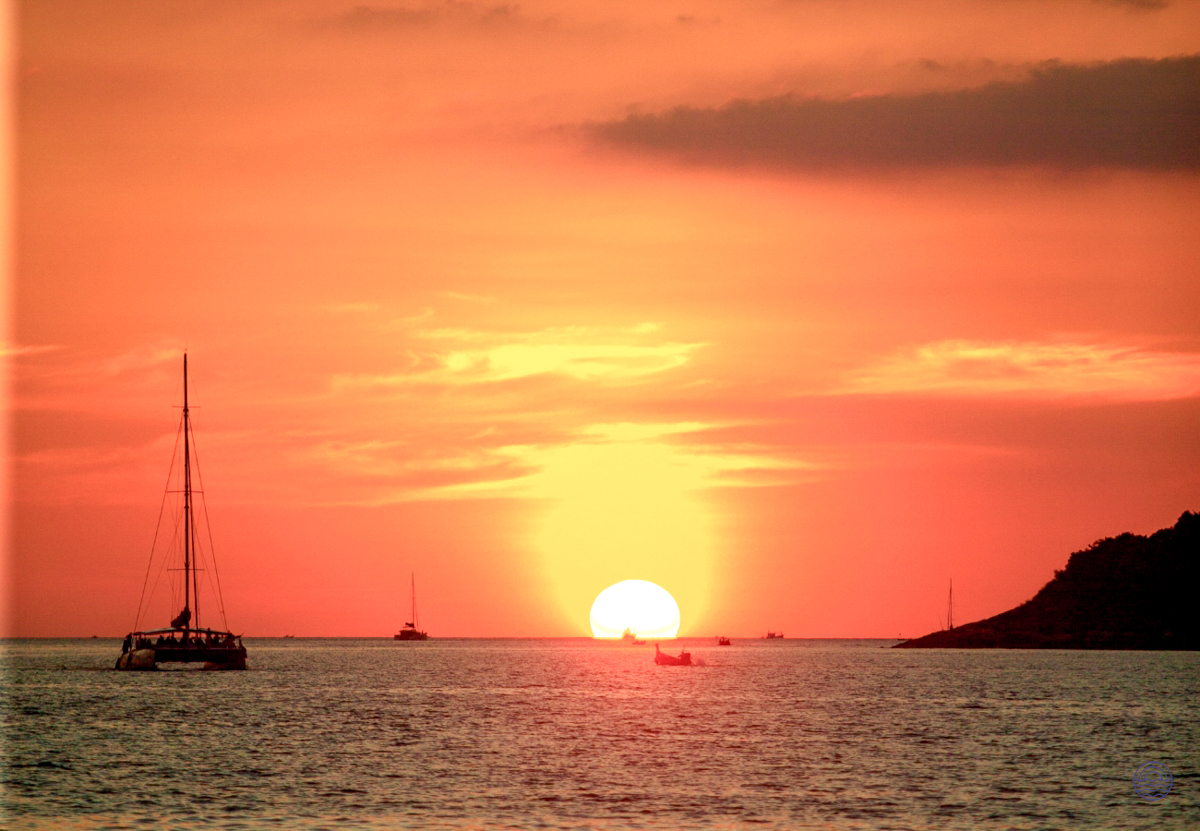 A breathtaking orange sunset over the Andaman Sea in Phuket, with boats silhouetted on the water.