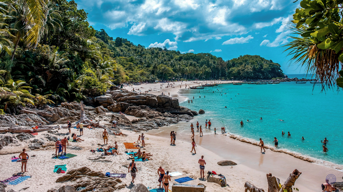 People enjoying the sun and turquoise waters on a beautiful sandy beach in Phuket.