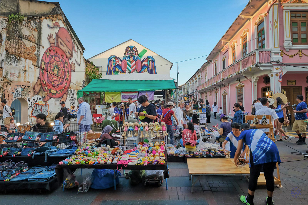 People enjoy browsing various goods at a bustling outdoor market in Phuket Old Town.