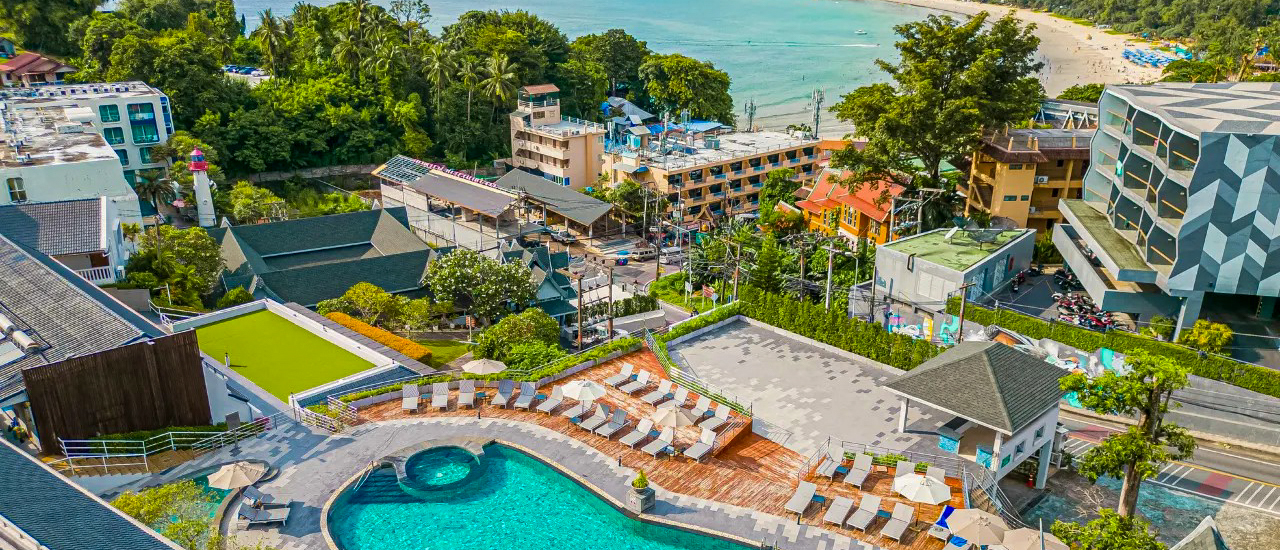 Tropical resort in Phuket with a large swimming pool, many sun loungers, and a beach.