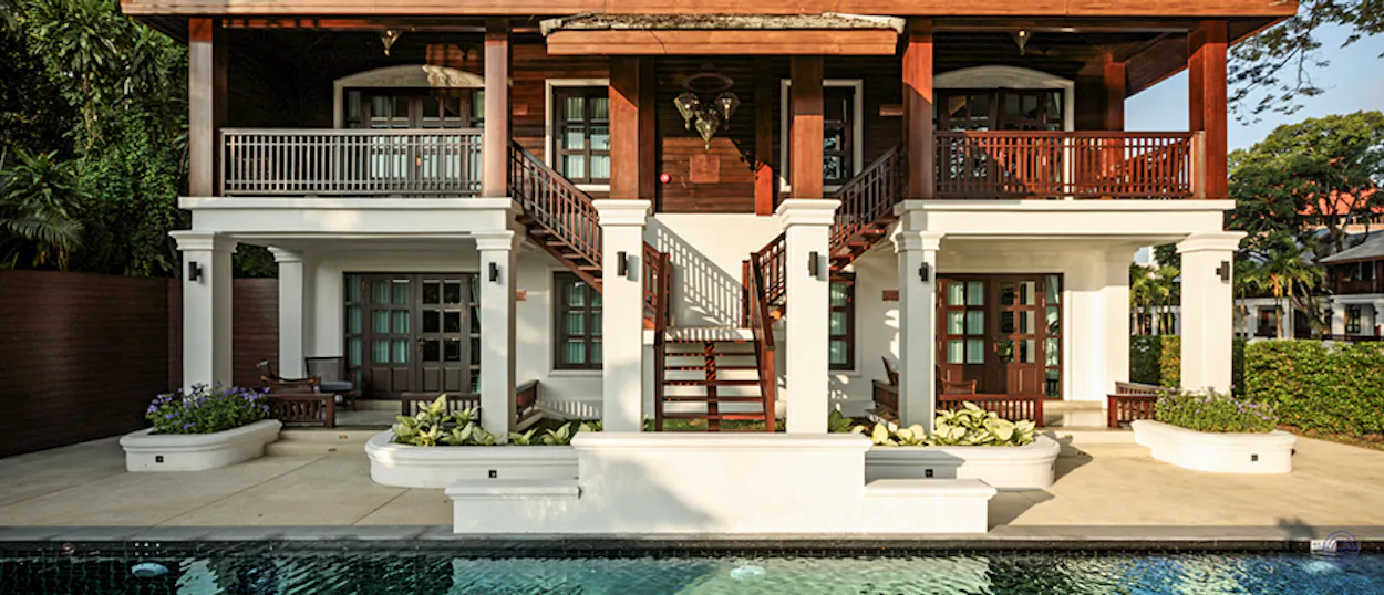 Luxurious traditional Thai resort with dark wood, white pillars, and a serene pool in Chiang Mai.