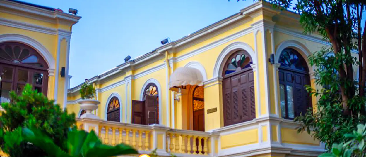 Elegant yellow historic building with arched windows and a balcony in Bangkok.