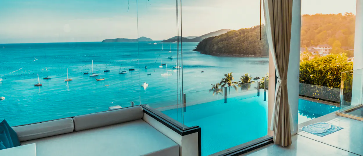 Luxury villa view with infinity pool and boats in a tropical bay at sunset in Phuket.