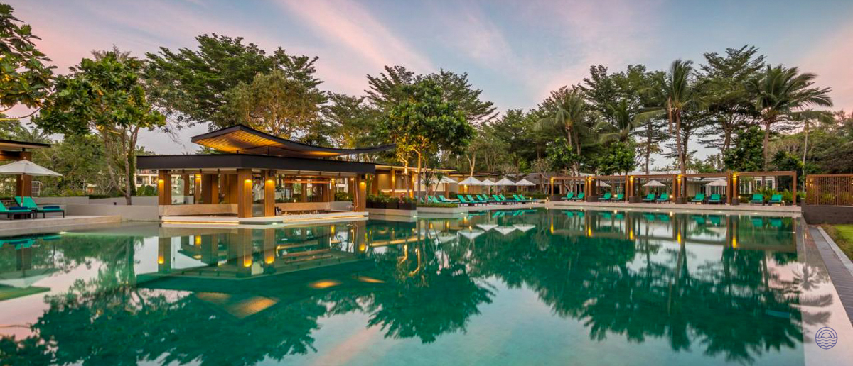 Luxurious resort swimming pool and bar area surrounded by tropical trees at sunset in Thailand.
