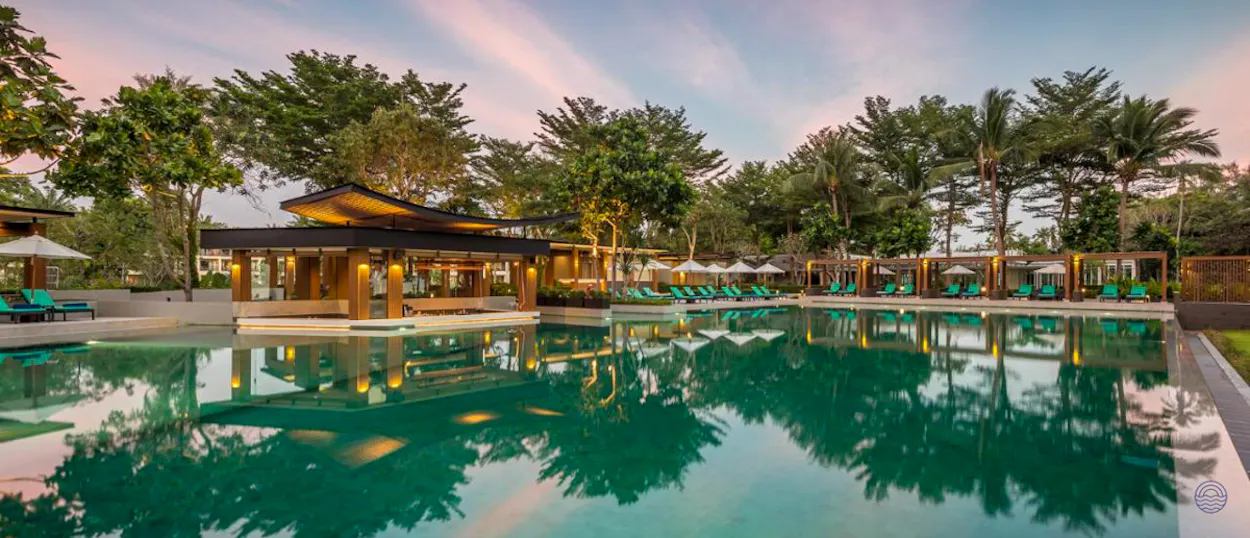 A tranquil resort swimming pool in Krabi with a poolside bar and lush tropical trees at sunset.