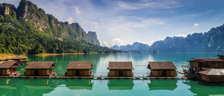 Traditional floating bungalows on a tranquil lake surrounded by majestic limestone mountains in Khao Sok, Thailand.