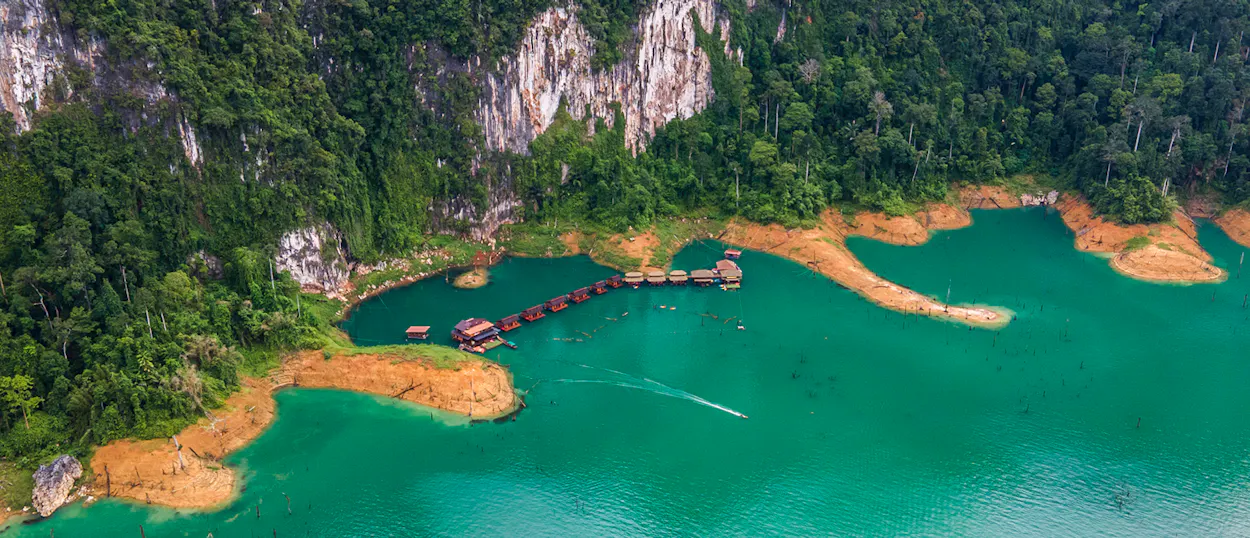 Floating bungalows on a serene turquoise lake in Khao Sok, Thailand, surrounded by lush jungle cliffs.