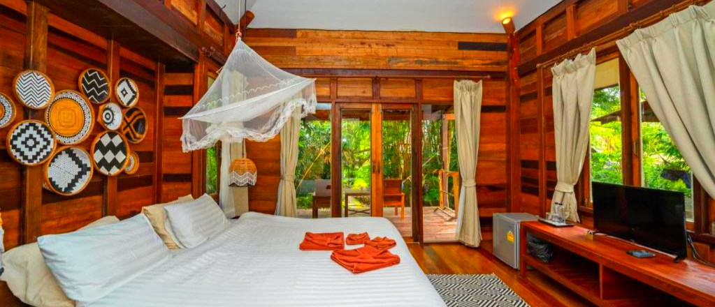 A serene wooden resort room on Koh Kood with a large bed, mosquito net, and lush tropical view.