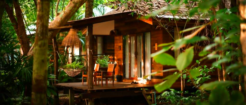 A tranquil wooden resort bungalow with a porch and hammock, surrounded by lush trees on Koh Kood.