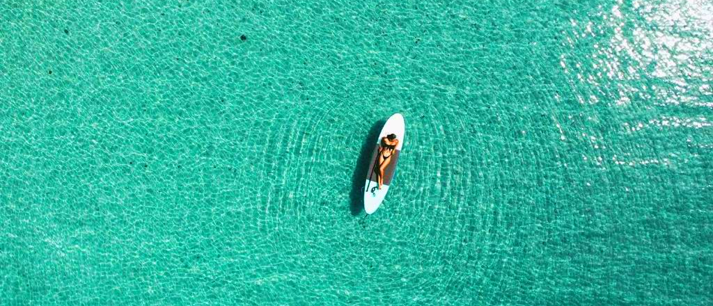 A person relaxes on a paddleboard, floating in the tranquil, crystal-clear turquoise waters of Koh Kood.