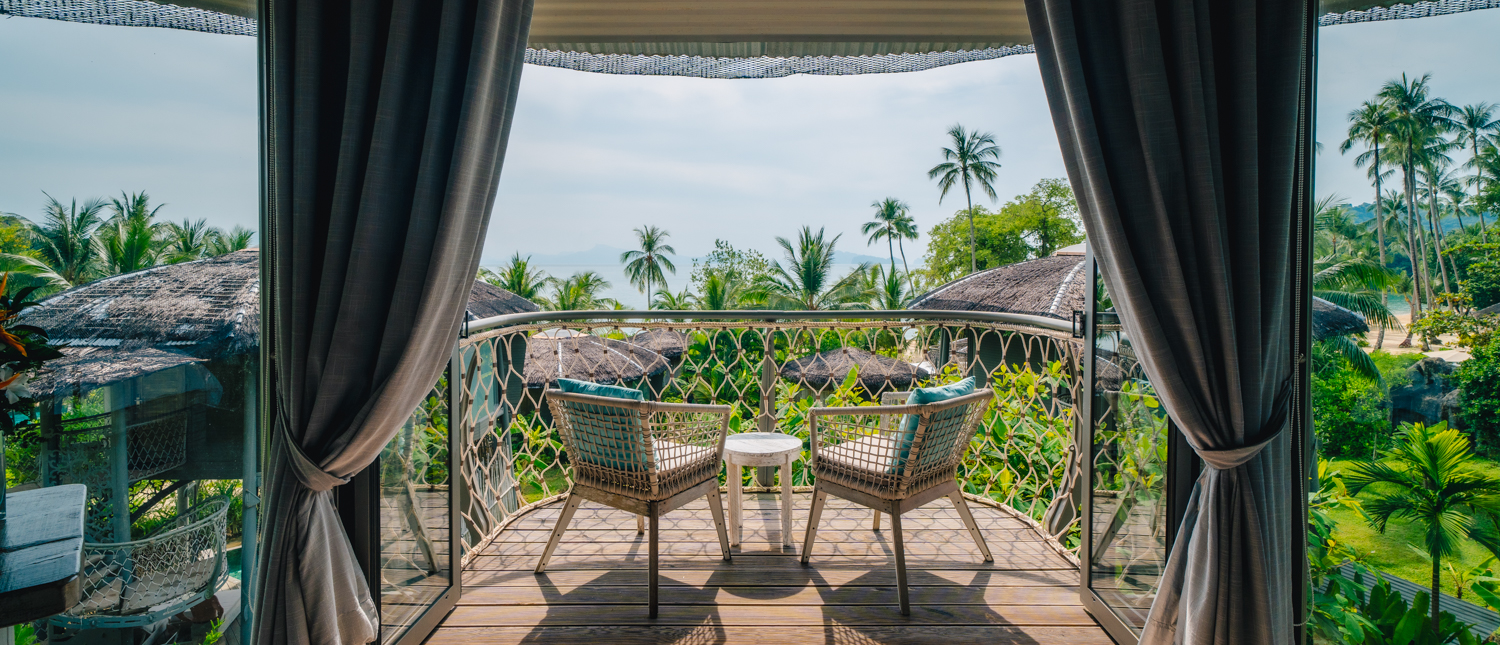 A serene balcony with two chairs overlooking lush tropical foliage and a beach on Koh Yao Noi.