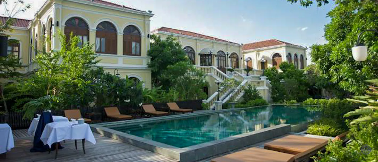 Elegant yellow hotel with a sparkling swimming pool, lounge chairs, and lush tropical gardens in Bangkok.