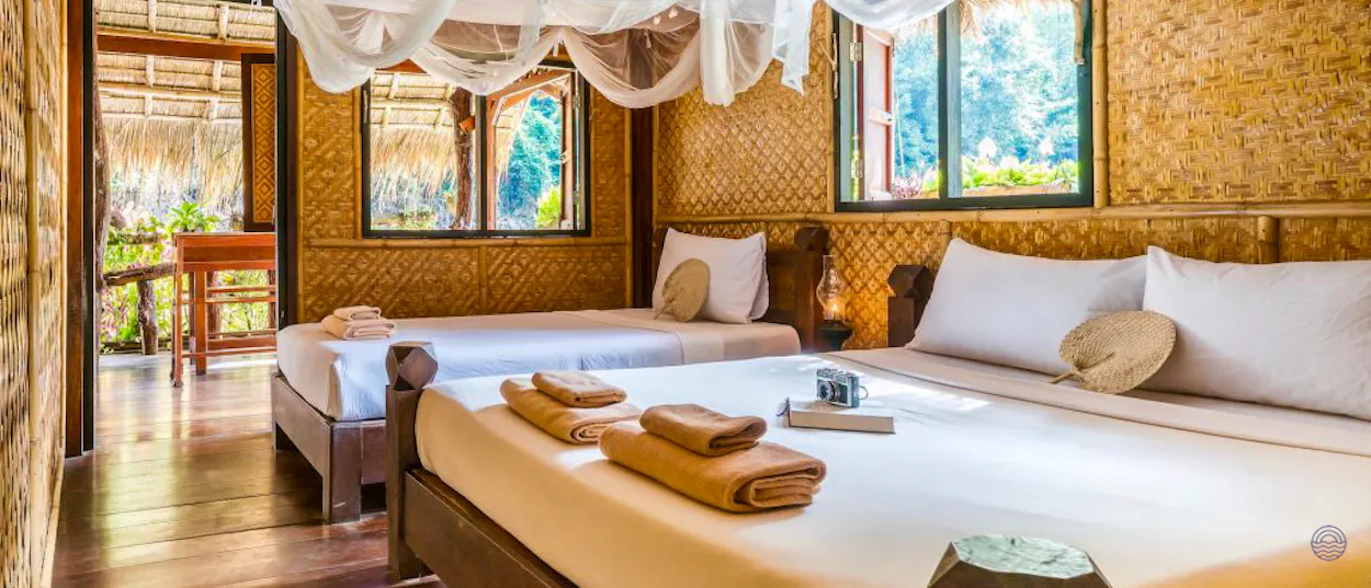 Rustic River Kwai bungalow room with two beds, mosquito nets, and views of dense jungle.