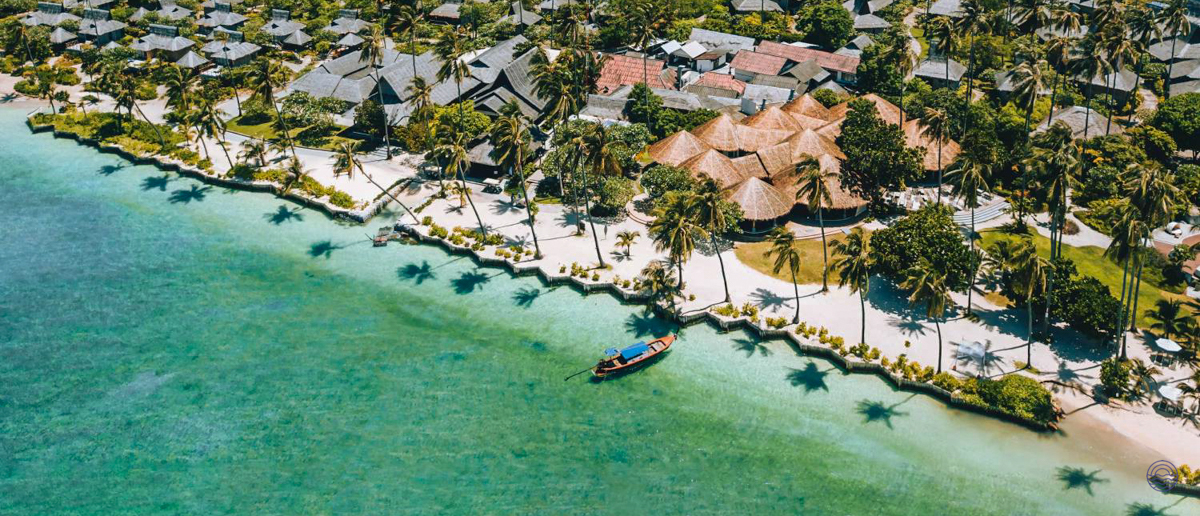 Aerial view of a beautiful Thai beach resort with palm trees and a longtail boat in turquoise water.