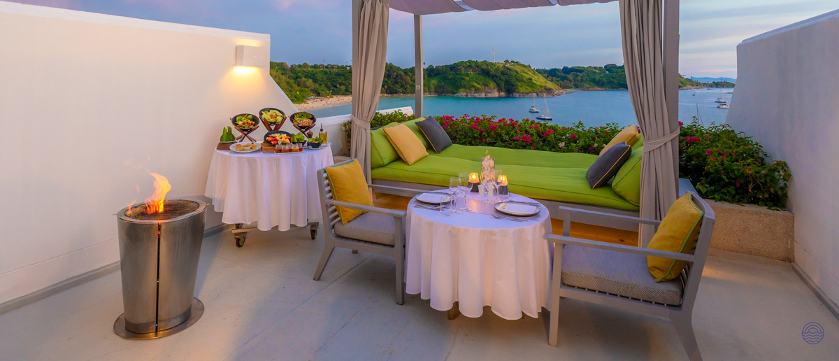Romantic rooftop terrace with private dinner, daybed, and fire pit overlooking a beautiful bay in Thailand.