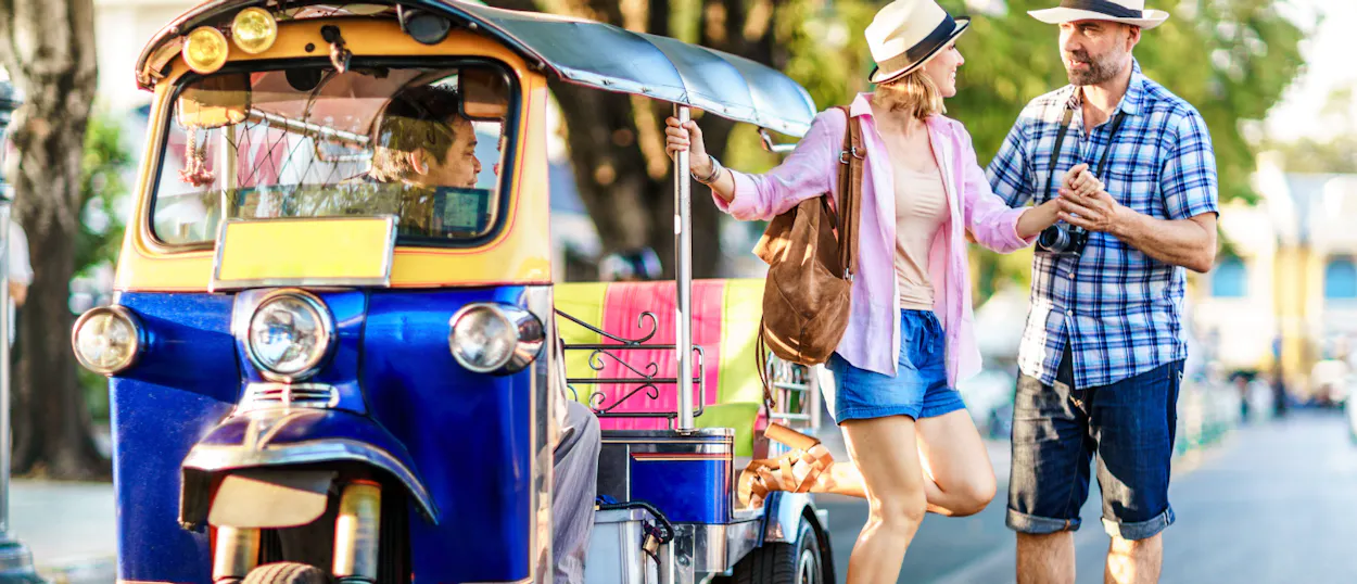 Tourists getting into a colorful tuk-tuk on a sunny street in Bangkok, ready for adventure.