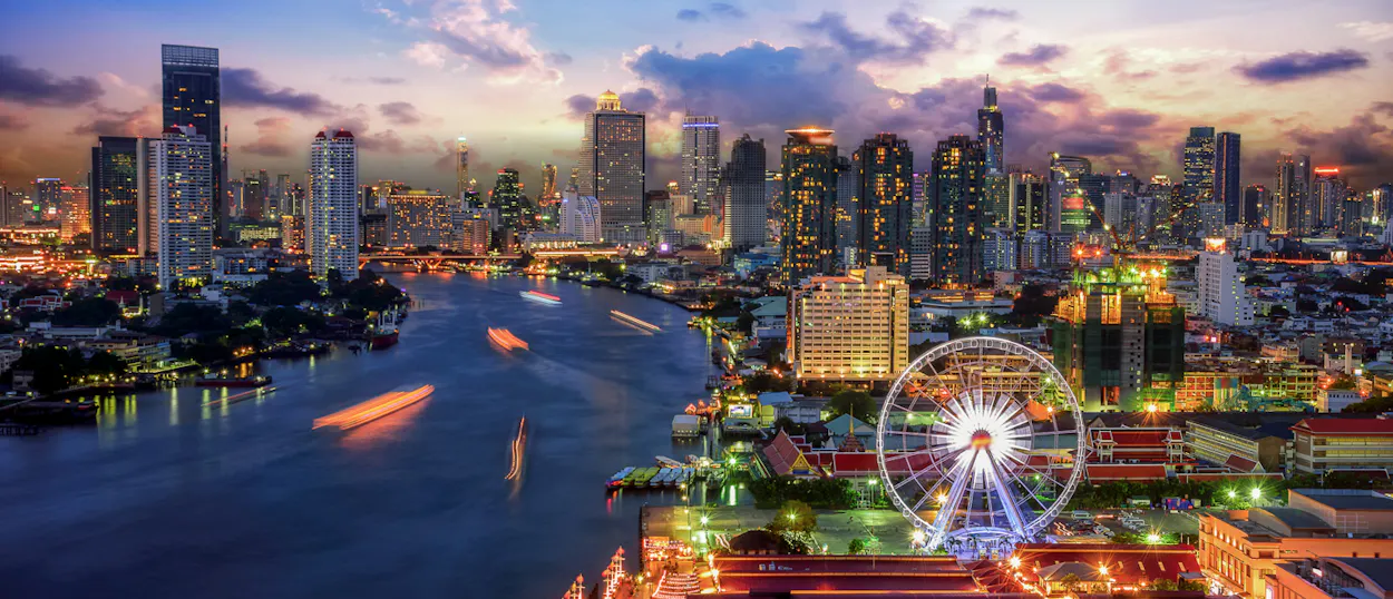 Vibrant Bangkok skyline at dusk, with the river, illuminated skyscrapers, and a glowing Ferris wheel.