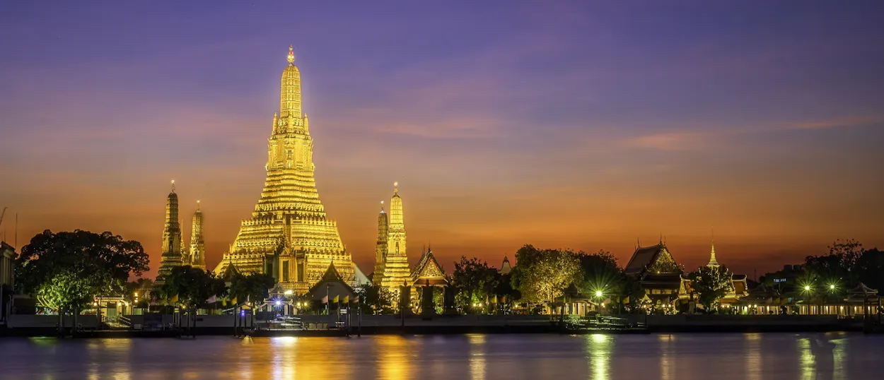 Bangkok's iconic Wat Arun temple shines brightly at dusk, its golden spires reflecting in the river.