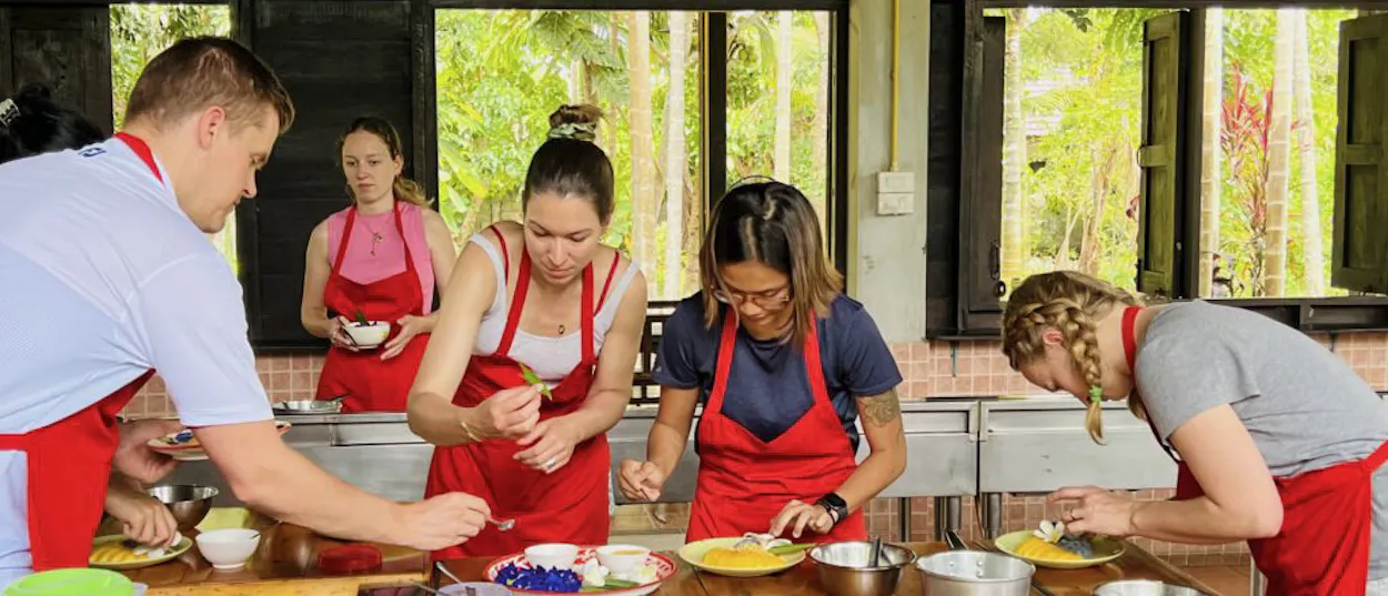 Travelers in red aprons learn to prepare fresh ingredients at a Thai cooking class in Chiang Mai.