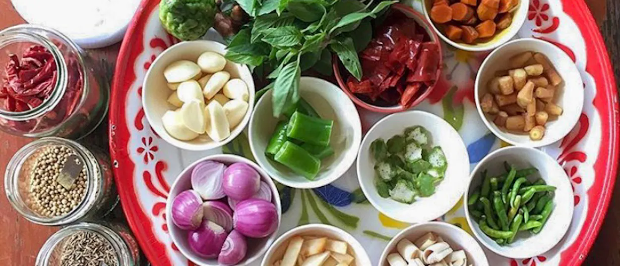 A colorful tray of fresh Thai cooking ingredients including garlic, chilies, and basil in Chiang Mai.