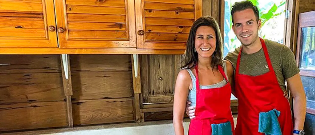 A happy couple in red aprons at a hands-on Thai cooking class in Chiang Mai.