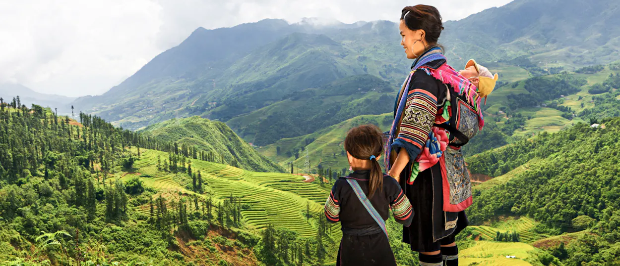 A Hmong woman and child in traditional dress admire the lush green mountain landscape in Chiang Mai.