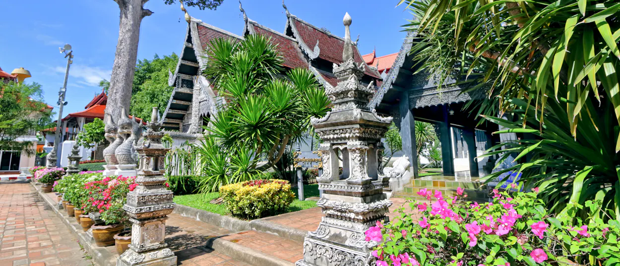 Traditional Thai temple in Chiang Mai featuring ornate roofs, stone carvings, and colorful tropical plants.