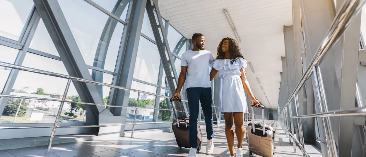 A happy couple walks through a modern airport terminal, pulling their luggage.