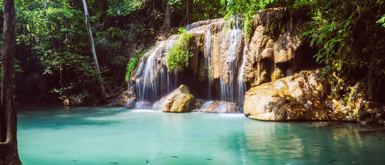 Erawan Waterfalls in Kanchanaburi, Thailand, cascade into a vibrant turquoise pool surrounded by lush jungle.