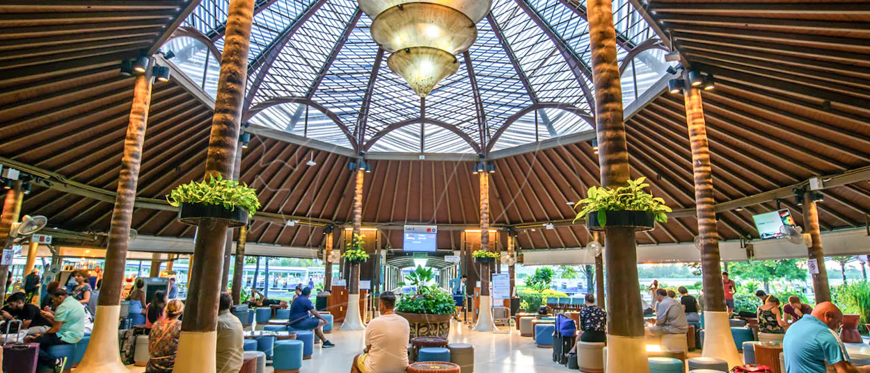 Relaxed travelers wait in the distinctive open-air terminal of Koh Samui airport, featuring palm-like columns.