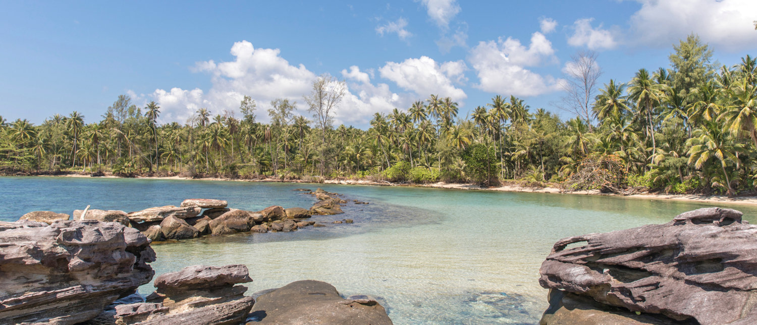 Large rocks frame a tranquil bay with clear turquoise water and a palm-lined beach on Koh Kood.