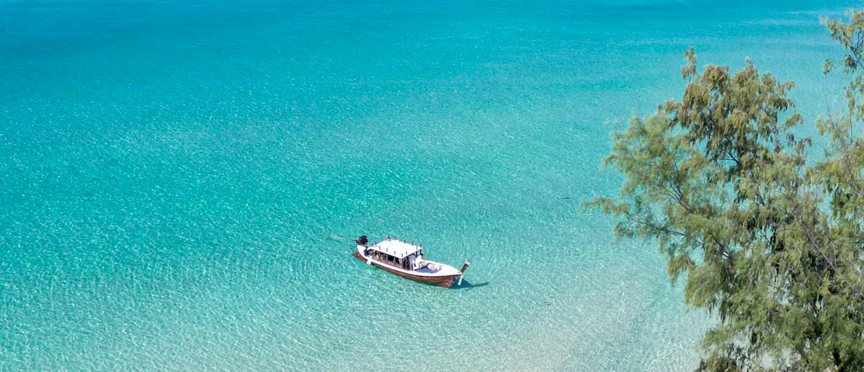 A longtail boat floats in the crystal-clear turquoise waters of Koh Kood, Thailand.