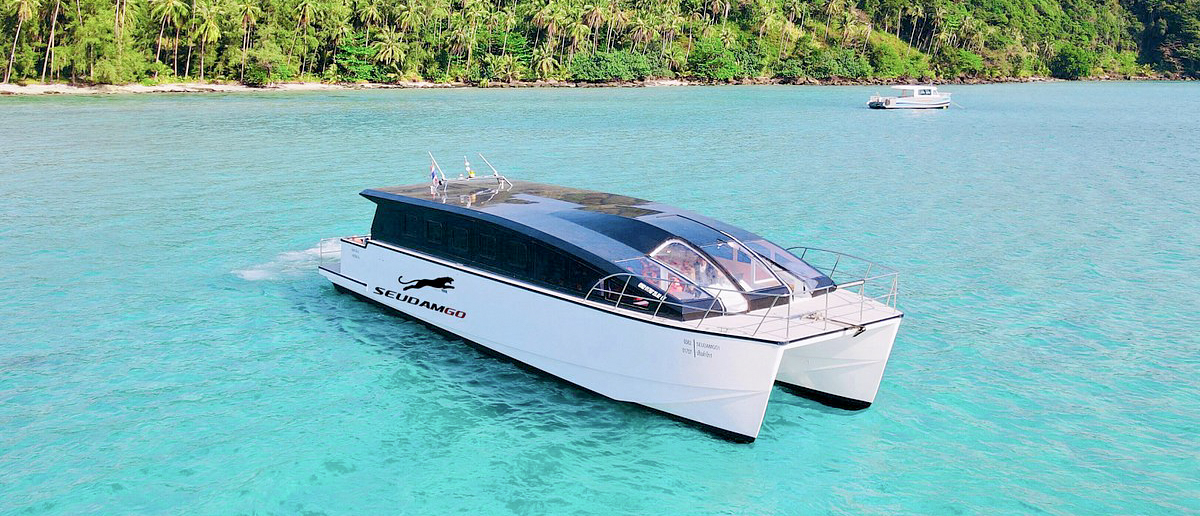 A modern white catamaran with a dark roof glides over the clear turquoise waters of Koh Kood.