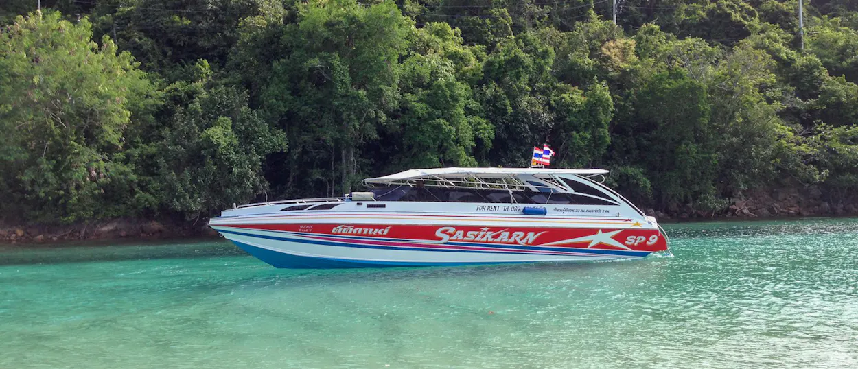 A speedboat with a Thai flag cruises on turquoise waters near lush green islands in Koh Phi Phi.