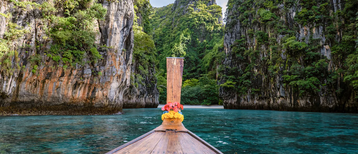 Sailing on a traditional longtail boat through crystal-clear waters surrounded by towering limestone cliffs in Koh Phi Phi.
