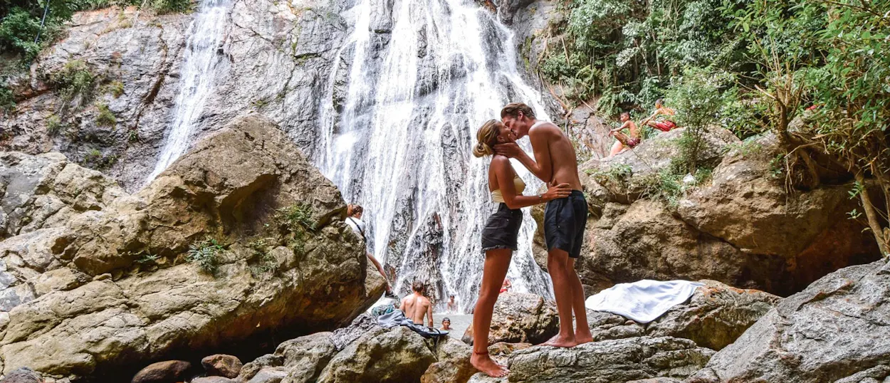 A loving couple shares a kiss by the majestic Na Muang waterfall on Koh Samui.