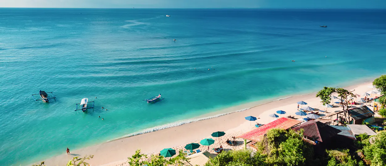 Beautiful Phuket beach from above, featuring calm turquoise water, boats, and beach umbrellas.