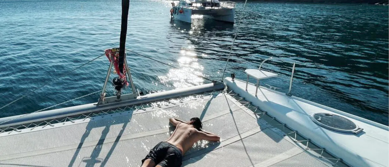 A person sunbathing on a catamaran net over the sparkling blue waters near Phuket.