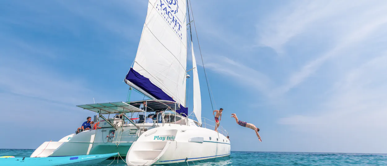 Excited travelers dive from a catamaran into the clear blue waters of Phuket, Thailand.