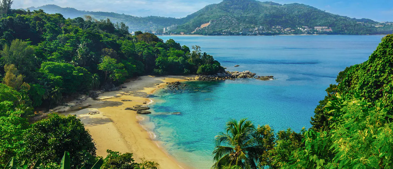 Beautiful tropical beach with golden sand, clear turquoise water, and lush green hills in Phuket.