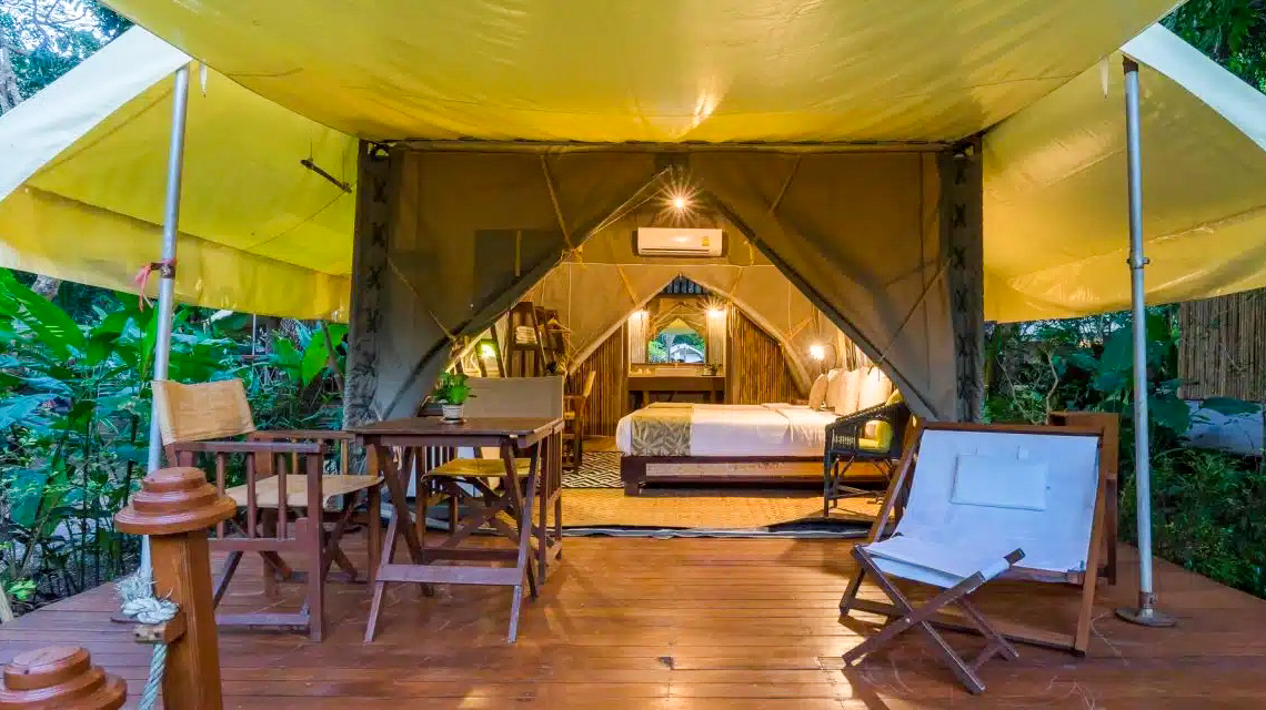 Luxurious glamping tent with a comfortable bed and outdoor deck in a tropical setting.