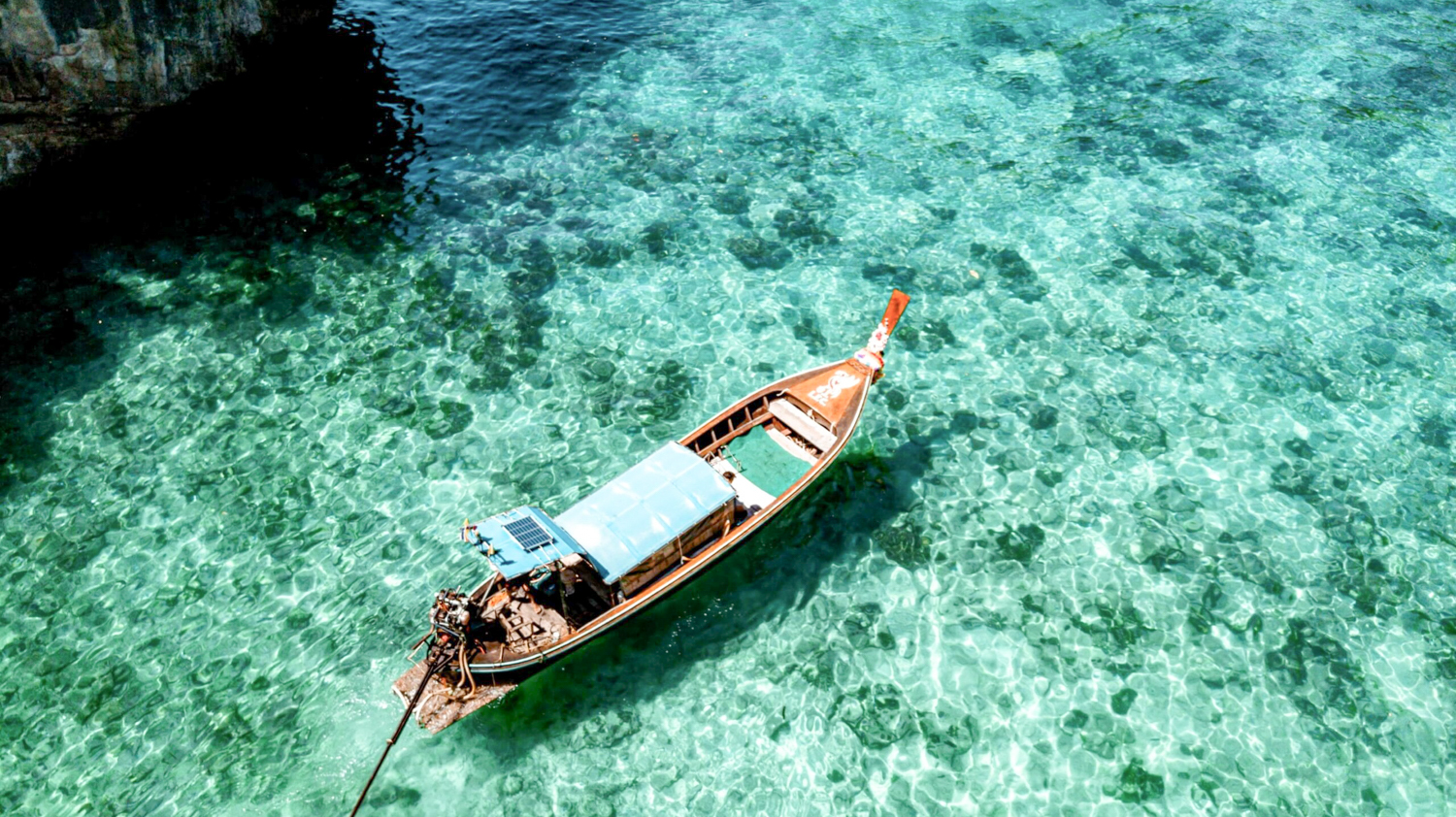 A traditional Thai longtail boat floats on crystal-clear turquoise water near a tropical island.