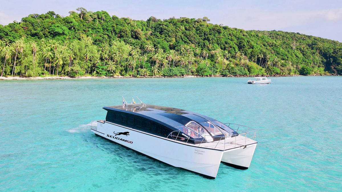 A sleek white catamaran floats on clear turquoise water near a lush tropical island in Koh Kood, Thailand.