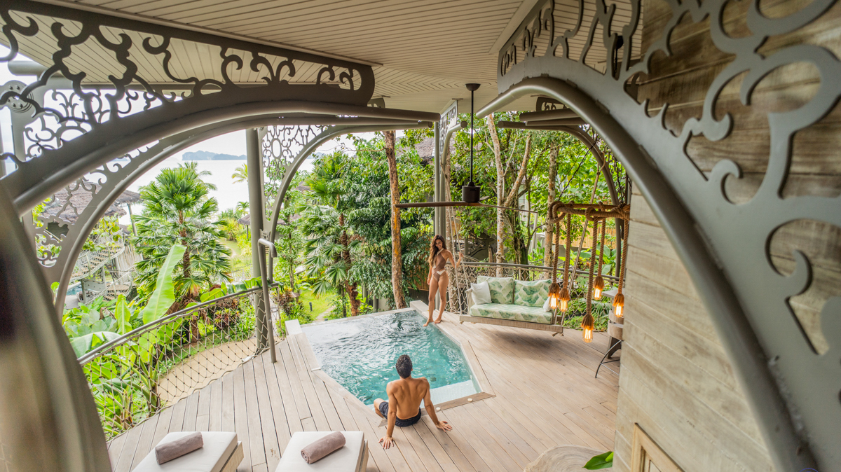 Couple relaxing by a private infinity pool on a luxurious treehouse balcony in tropical Thailand.