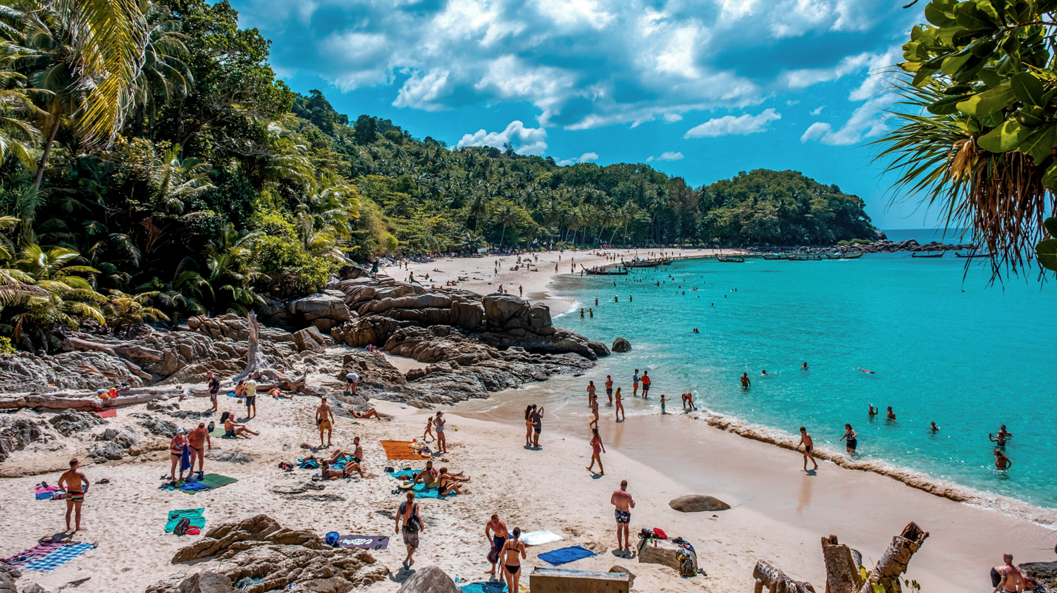 Many people enjoying the sunny white sand beach and clear turquoise waters of Phuket, Thailand.