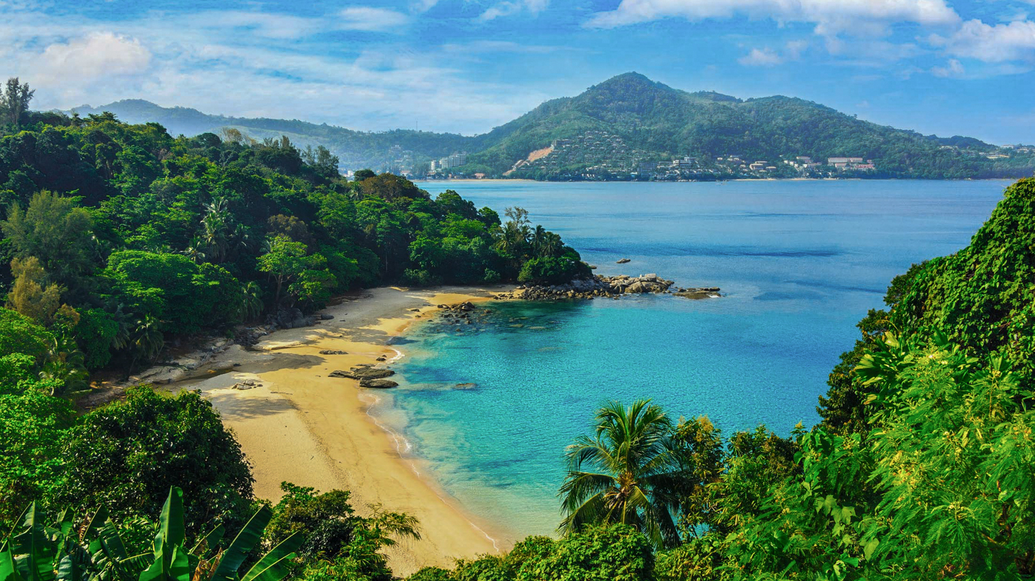 Beautiful Phuket beach in Thailand with clear turquoise water, golden sand, and lush green jungle.