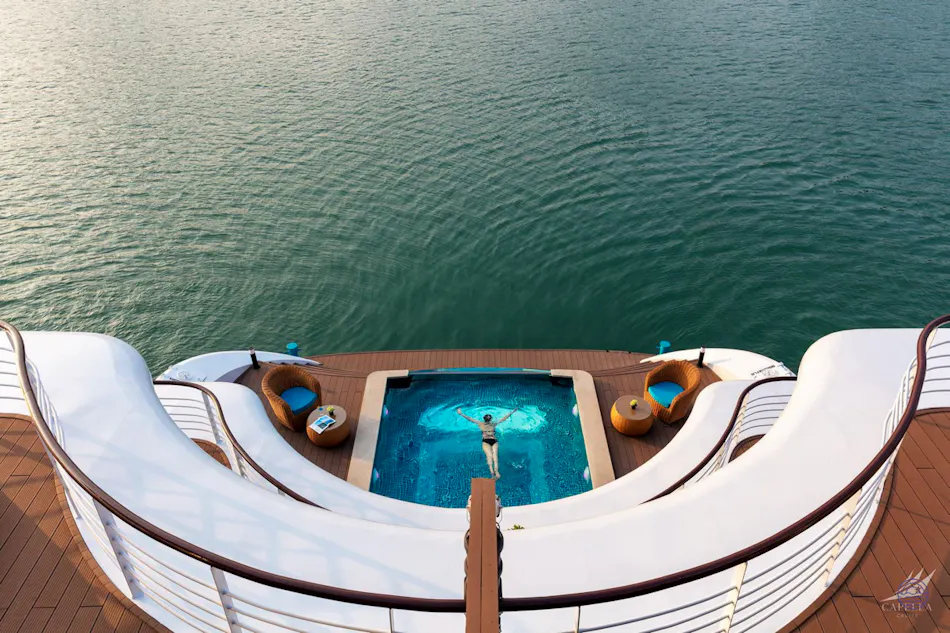 A person swims in a luxurious pool on a cruise ship deck overlooking calm Ha Long Bay waters.