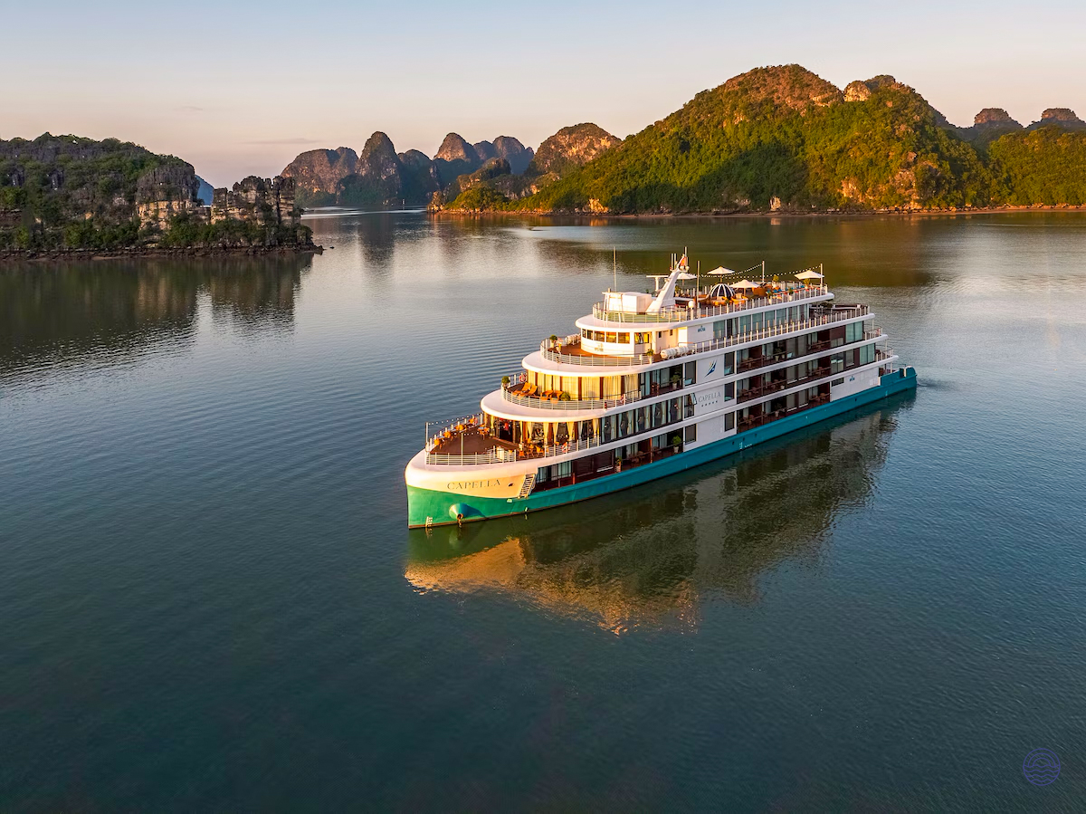 A beautiful cruise ship glides through the serene waters of Ha Long Bay at sunset.