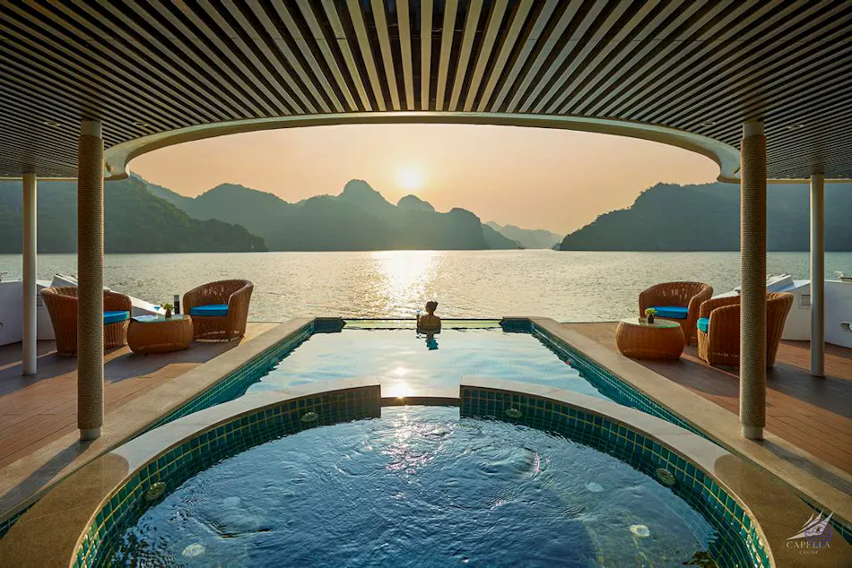 A person relaxes in an infinity pool on a cruise ship overlooking Ha Long Bay at sunset.